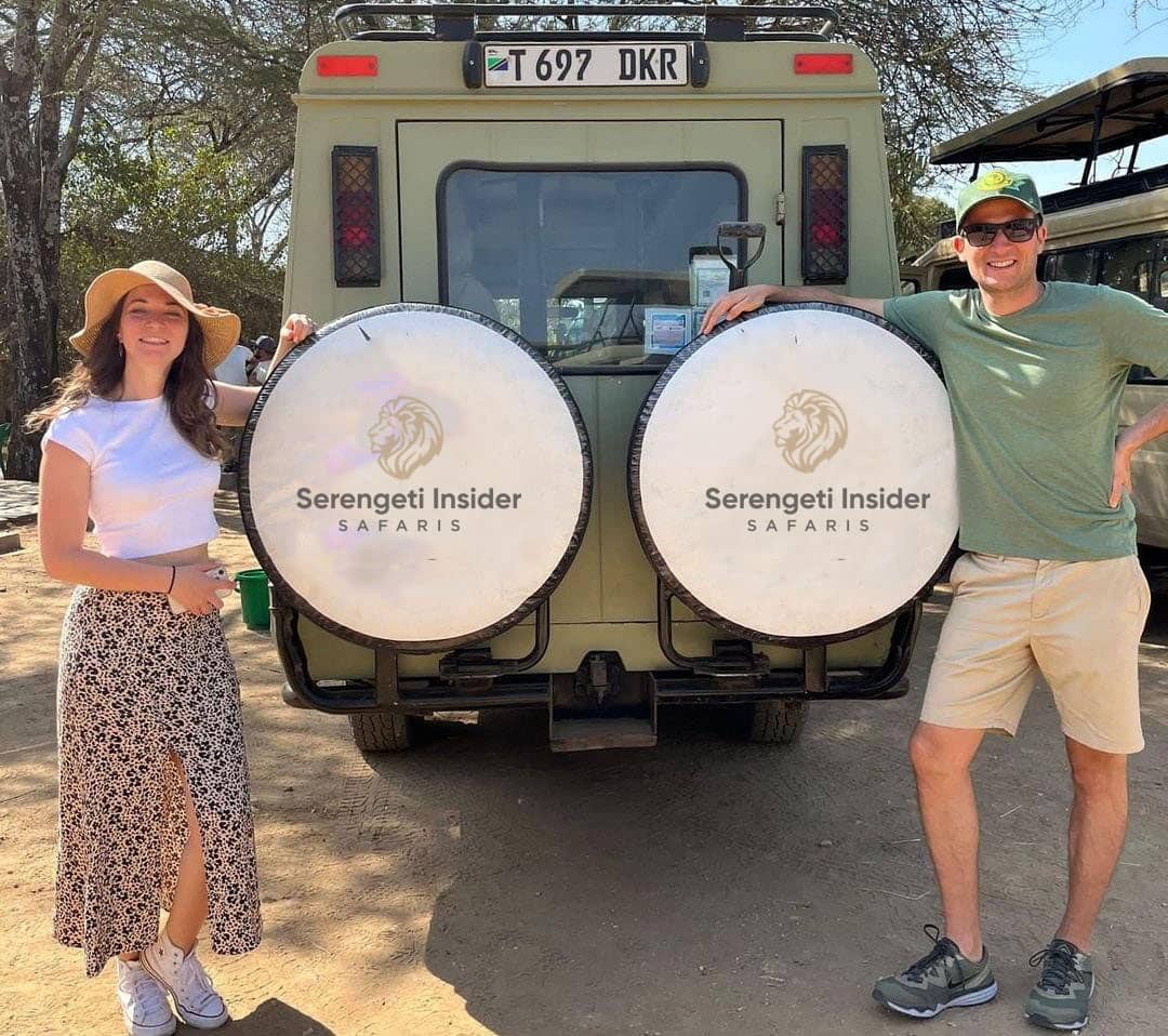 Tourists standing outside a safari truck with a Serengeti Insider Safaris, surrounded by the Serengeti landscape.
