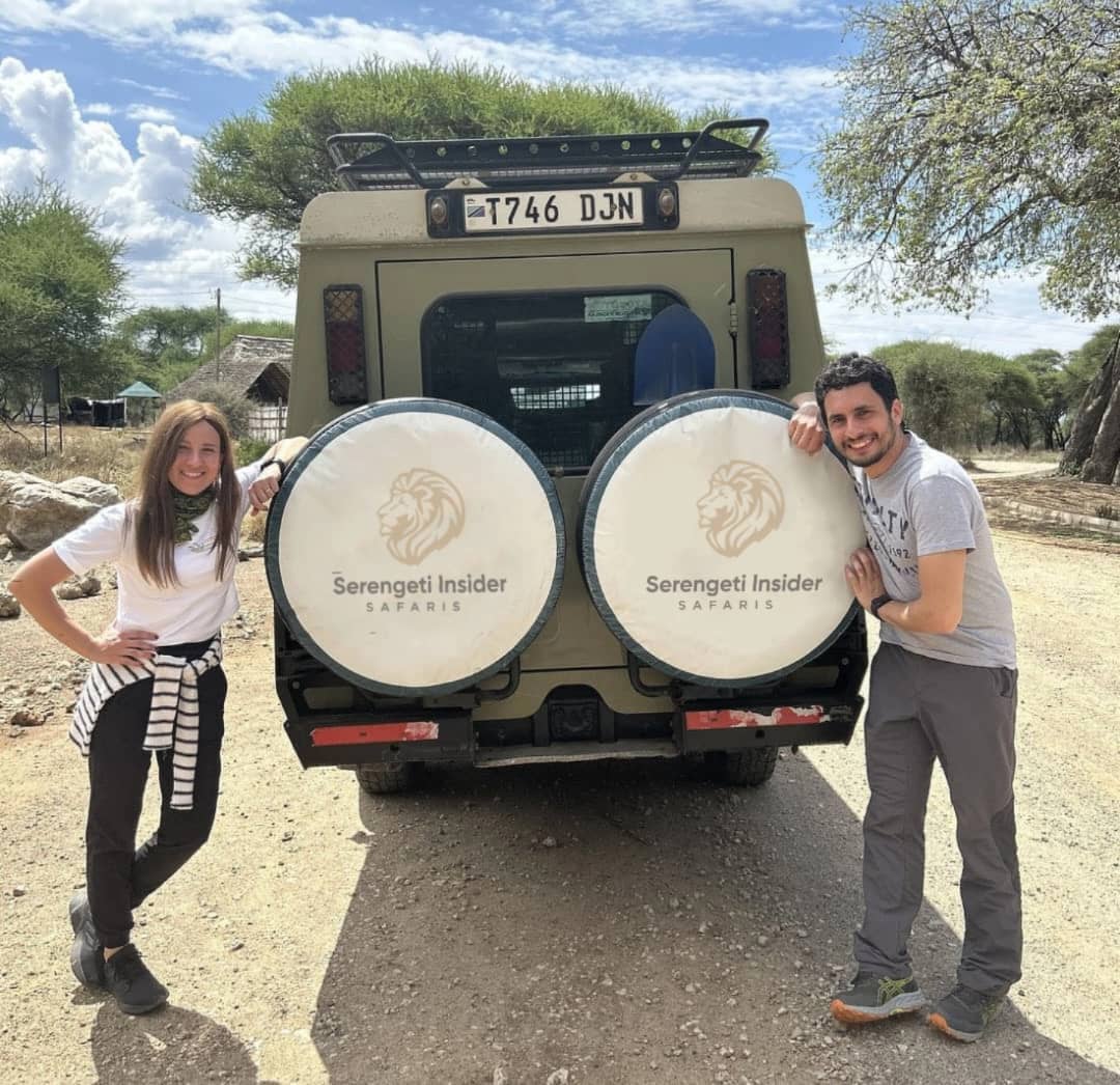 Tourists posing for a group photo behind a safari vehicle in Tanzania.